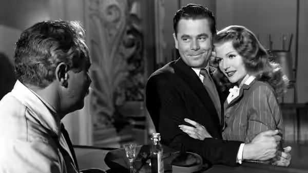 Johnny Farrell (Glenn Ford) embraces Gilda (Rita Hayworth) as a man watches