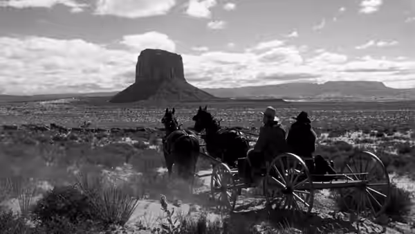 A covered wagon and riders cross a wide, open desert plain