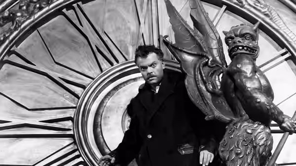 Charles Rankin (Orson Welles) stands beside a large carved statue beneath a circular window
