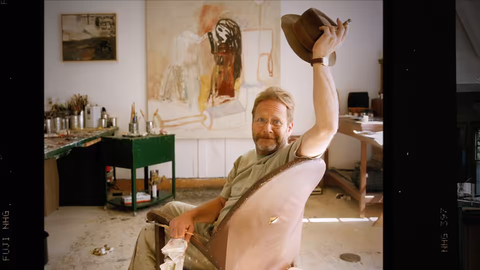 Self (Martin Mull) raises a hat while seated in a kitchen