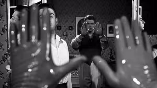 A man raises his hands before a mirror as others watch from the room