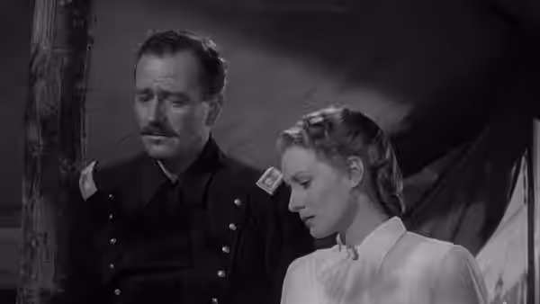 Kirby Yorke (John Wayne) stands beside Kathleen Yorke (Maureen O’Hara) indoors