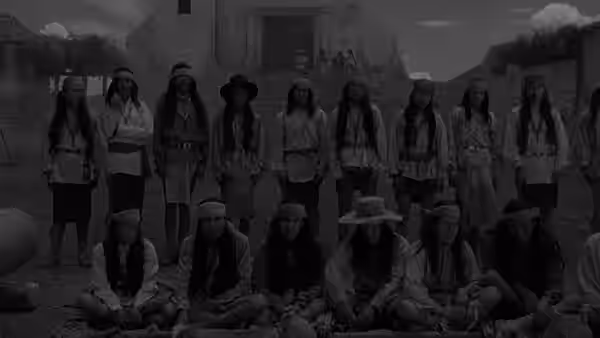 Women and children stand and sit in rows outside an adobe building