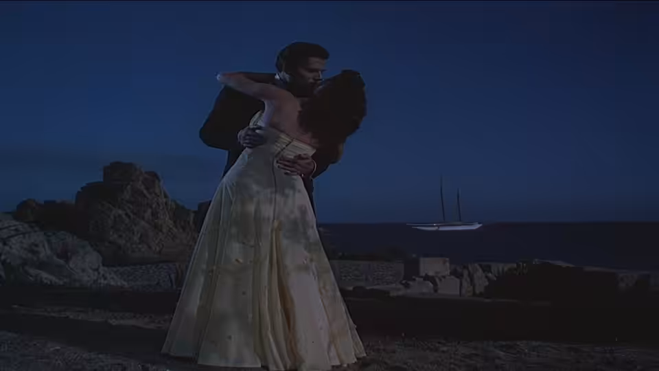 A man and woman embrace on a rocky shoreline after dark
