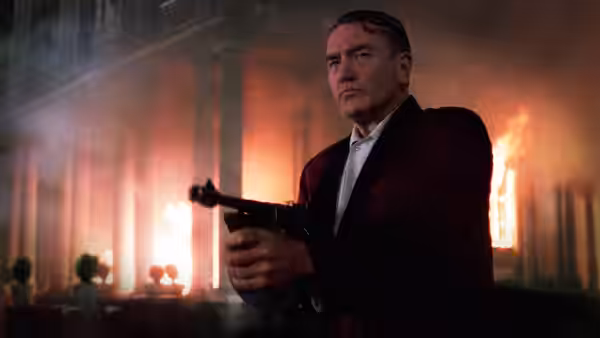 Leo (Albert Finney) holding a pistol in front of a burning building at night