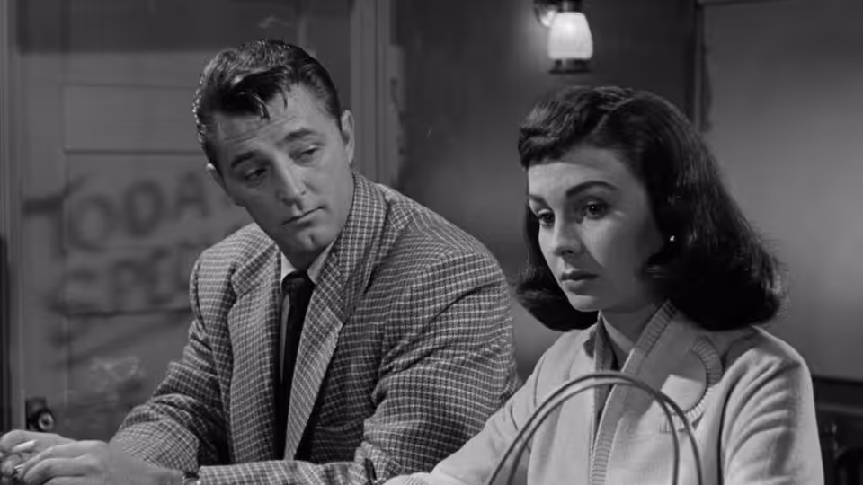 Frank Jessup (Robert Mitchum) watches Diane Tremayne (Jean Simmons) sitting beside him at a desk