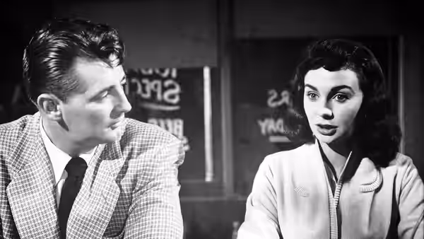 Frank Jessup (Robert Mitchum) turns toward Diane Tremayne (Jean Simmons) as they sit together indoors