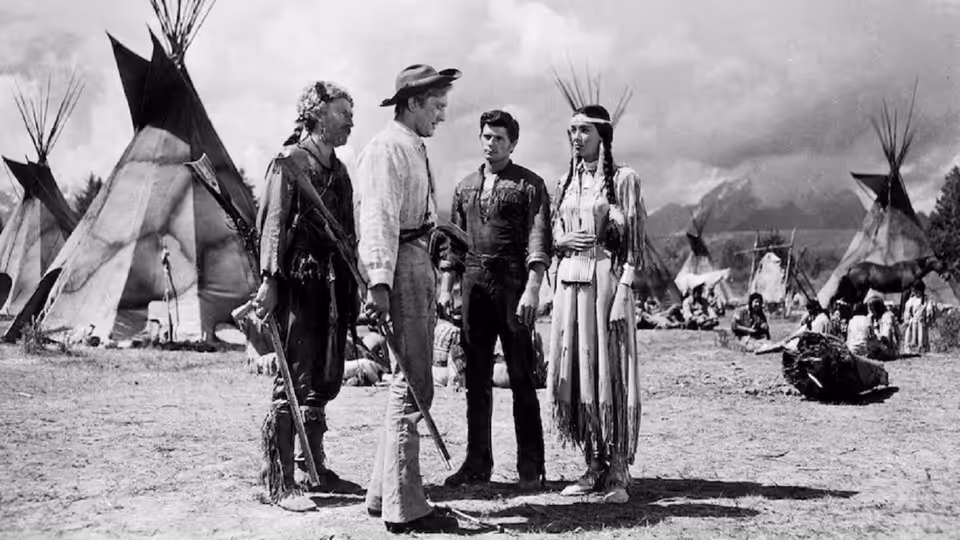 A frontier party stands among tipis at a Native encampment