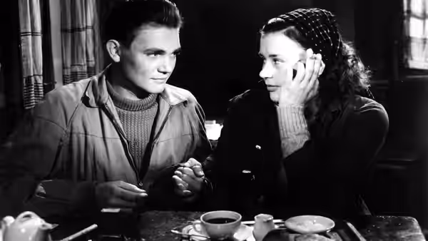 Harry (Lars Ekborg) and Monika (Harriet Andersson) sit together at a table indoors