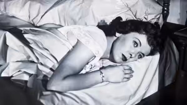 A woman lies awake in bed, clutching the sheet to her chest