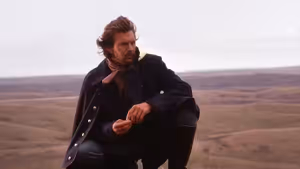 Lieutenant Dunbar (Kevin Costner) crouching in the grassland examining an item