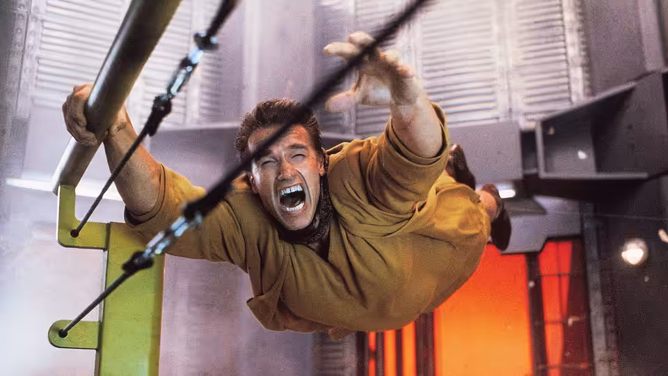 Quaid (Arnold Schwarzenegger) hanging from a metal beam while shouting