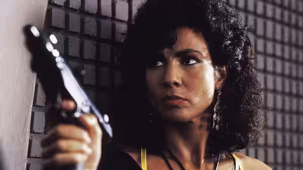 Melina (Rachel Ticotin) holding a pistol and looking to the side