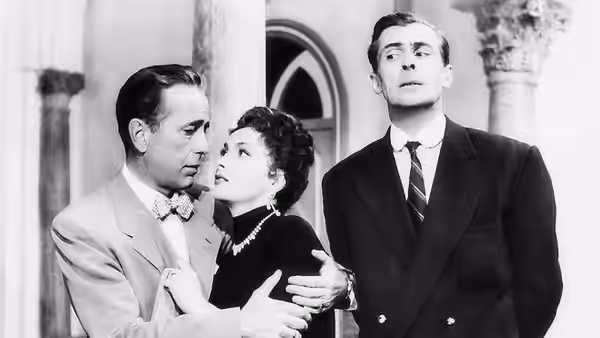 Billy Dannreuther (Humphrey Bogart) holds Maria Dannreuther (Gina Lollobrigida) close while Harry Chelm watches