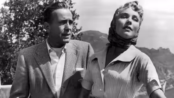Billy Dannreuther (Humphrey Bogart) walks beside a woman in a headscarf outdoors
