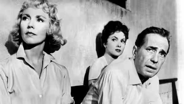 Billy Dannreuther (Humphrey Bogart) sits beside two women as they look off to the side