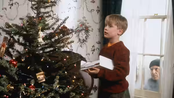 Kevin (Macaulay Culkin) holding papers by a Christmas tree as Marley watches