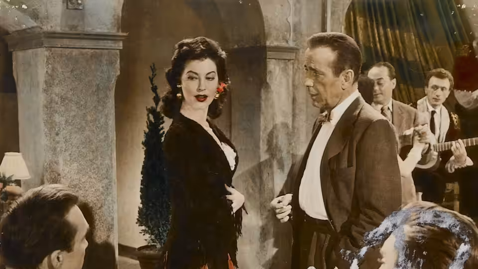 Maria Vargas (Ava Gardner) stands beside Harry Dawes (Humphrey Bogart) at a party