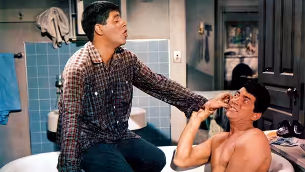 Eugene Fullstack (Jerry Lewis) reaches toward a reclining man in a bathtub