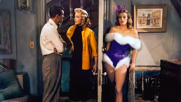 A man speaks with a blonde woman as a model in a purple outfit stands nearby