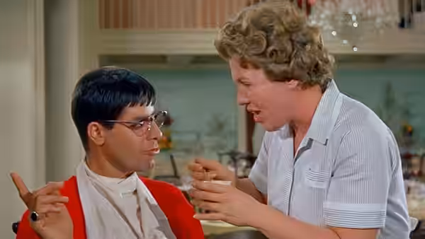 Herbert H. Heebert (Jerry Lewis) sits as a blond man leans toward him with a spoon