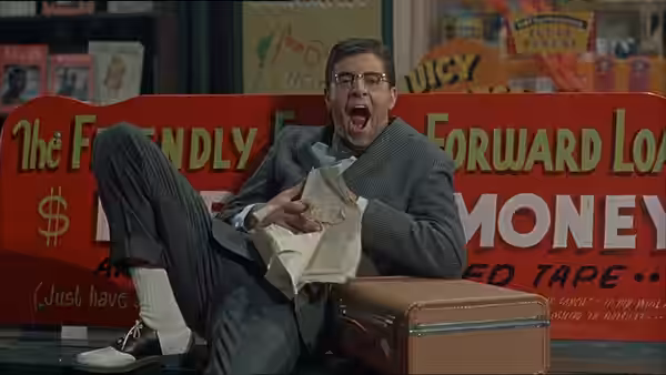 Herbert H. Heebert (Jerry Lewis) clutches a bundle of paper before a giant money sign