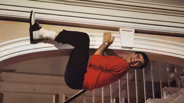 Herbert H. Heebert (Jerry Lewis) clings sideways to a wall in a red shirt