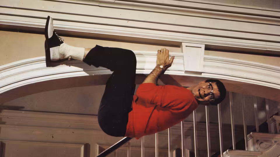 Herbert H. Heebert (Jerry Lewis) clings sideways to a wall in a red shirt
