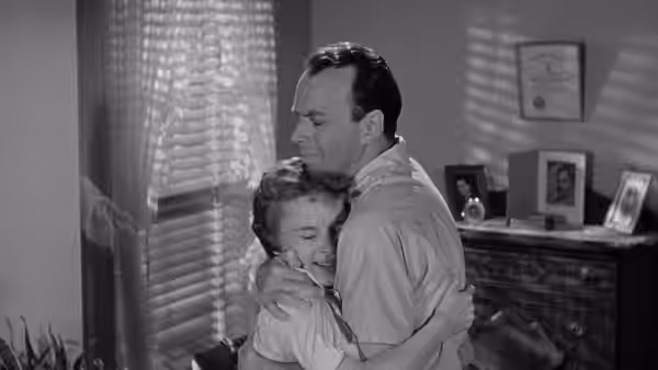 A man embraces a woman beside a mantel crowded with framed photographs