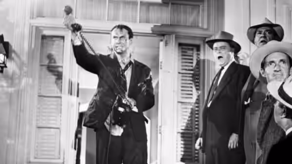 A man raises his arm before a group of men gathered in a doorway