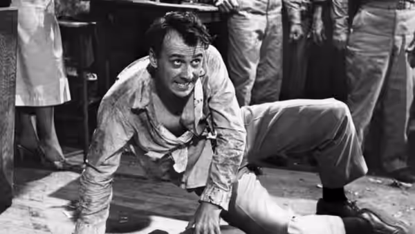 A dishevelled man crouches on the floor as others stand around him