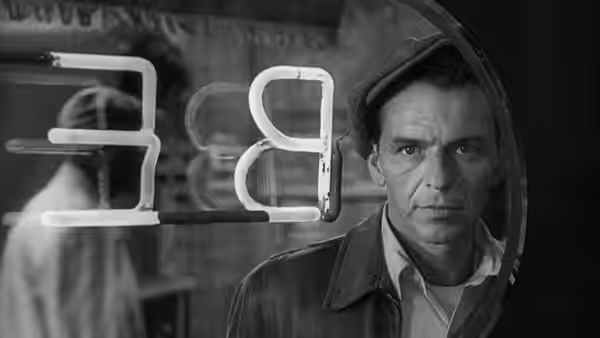 Frankie Machine (Frank Sinatra) stands behind a glowing neon sign