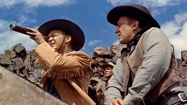 A cowboy points across rocky terrain as other men gather behind him