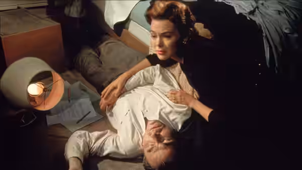 Lou Avery (Barbara Rush) holds Ed (James Mason) as he lies on the floor beside a desk
