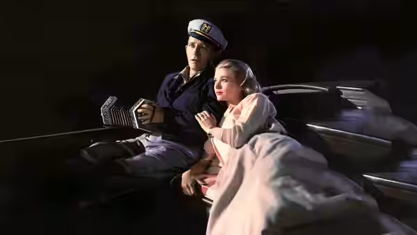A woman wrapped in a blanket rides beside a uniformed driver in a car at night