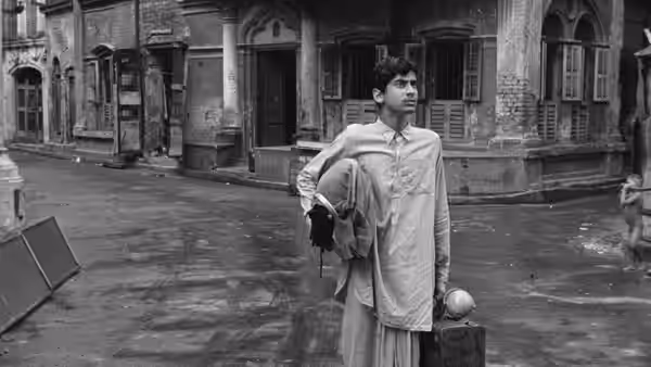 Teenage Apu Roy (Smaran Ghosal) stands with luggage on a city street