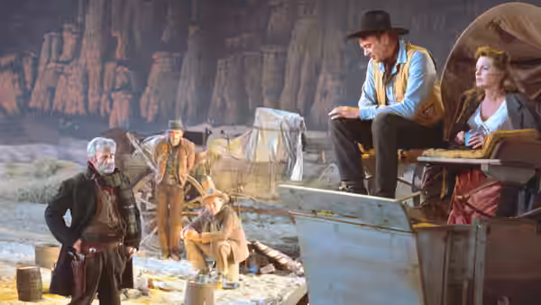 Link Jones (Gary Cooper) sits beside Billie Ellis (Julie London) on a wagon as men gather nearby
