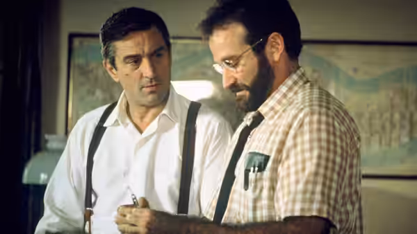 Malcolm Sayer (Robin Williams) standing beside a colleague holding a pen