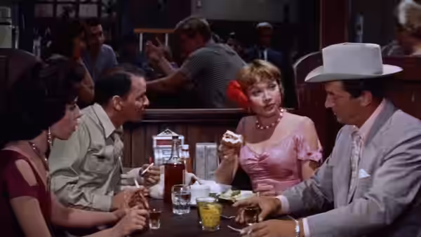 Bama Dillert (Dean Martin) sits at a bar with Ginnie Moorehead (Shirley MacLaine) and other patrons