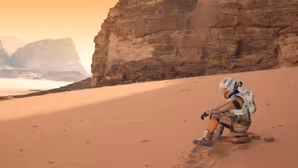 An astronaut in an orange spacesuit sits on a rock in a sandy desert