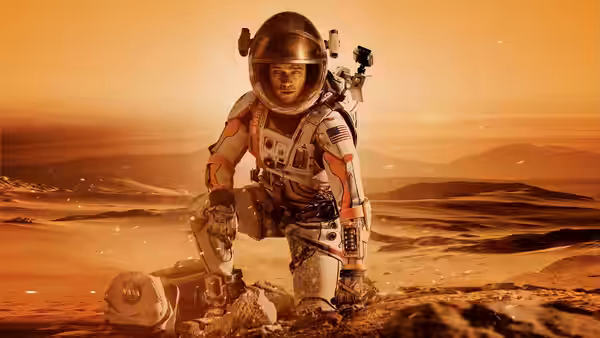 Mark Watney (Matt Damon) kneels on rocky ground holding equipment in the desert