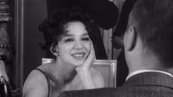 A smiling woman rests her cheek on her hand across the table from a man