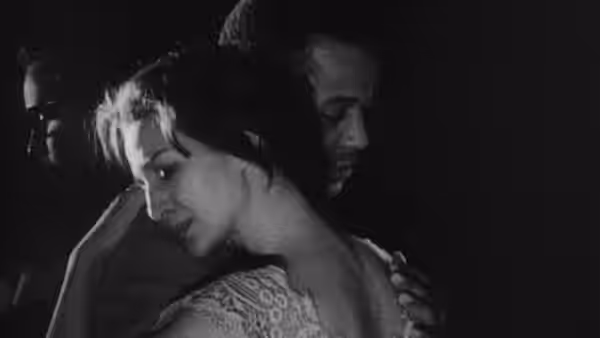 A woman leans forward while a man stands close behind her in the dark