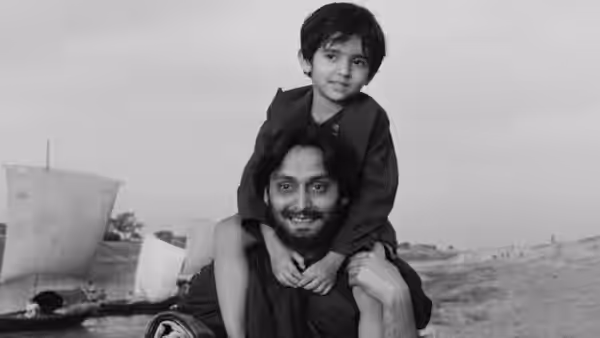A man carries a boy on his shoulders beside a river