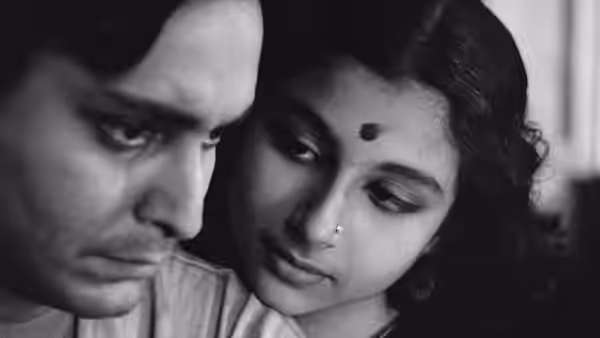 A man and woman sit close together, looking down thoughtfully