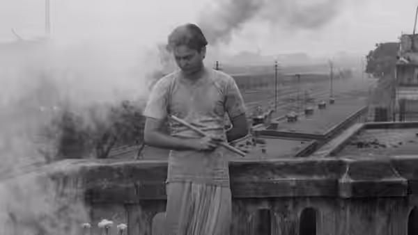A man stands on a rooftop holding a bundle of sticks