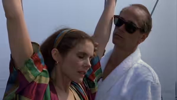 A man in sunglasses and robe beside a woman with arms raised outdoors