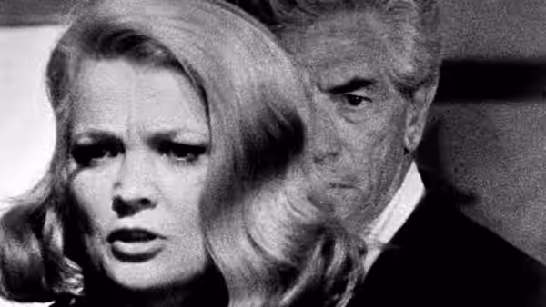 A blonde woman faces forward as a gray-haired man stands behind her