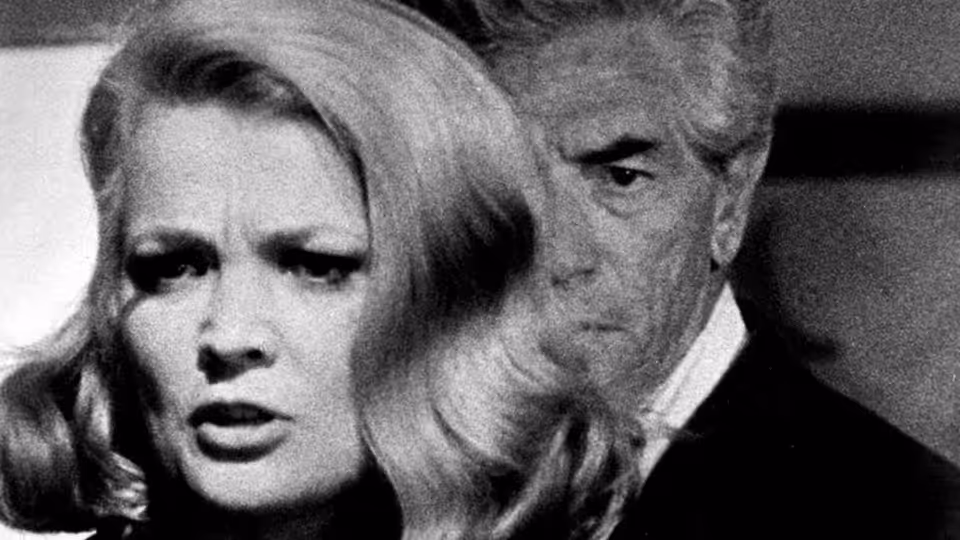A blonde woman faces forward as a gray-haired man stands behind her