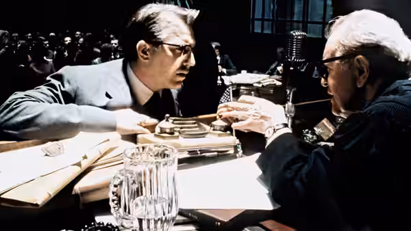 Two suited men conferring over papers at a hearing table